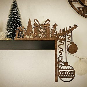 以下が含まれることがあります： ギフトボックス、クリスマスツリー、オーナメントが特徴の木製のクリスマスをテーマにした棚の装飾。茶色の装飾は素朴な外観です。小さな緑色のクリスマスツリーも存在します。白い球形のライトが吊り下げられています。