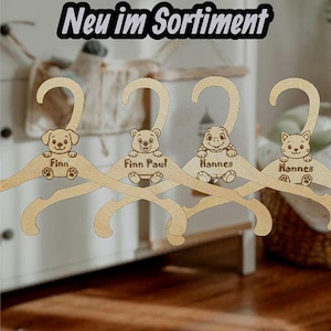 Könnte beinhalten: Kinderkleiderbügel aus Holz mit Tiermotiven: ein Hund, ein Bär, eine Schildkröte und eine Katze. Jeder Bügel hat einen eingravierten Namen. Der Text "Neu im Sortiment" steht oben. Die Bügel sind aus hellem Holz.