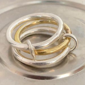 May include: A collection of silver and gold rings. The rings are stacked together, with a mix of silver and gold bands. The rings are on a silver plate. The rings have a simple, elegant design.