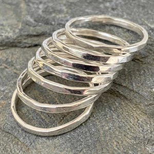 May include: A stack of six silver rings, each featuring a hammered, textured surface. The rings are arranged in a cascading formation, showing their circular bands and reflective metallic finish. The silver material has a bright, polished appearance.