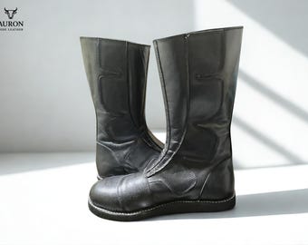 May include: A pair of black leather boots with a knee-high shaft and a zipper closure. The boots have a rounded toe and a thick sole. The brand logo "AURON HIDE LEATHER" is visible in the upper left corner.