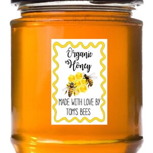 May include: A glass jar filled with honey, labeled "Organic Honey" with a bee and honeycomb design. The label also reads "Made with love by Tom's Bees".
