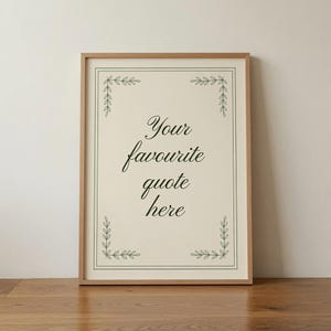 May include: A rectangular wall art print in a light wood frame featuring a cream-colored background with a thin dark green border and decorative leaf motifs in each corner. The text "Your favourite quote here" is printed in a dark green script font.