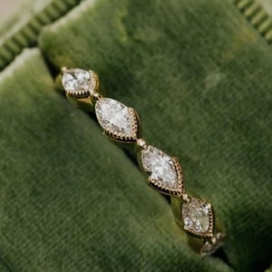 Könnte beinhalten: Ein goldener Ring mit Diamanten im Marquiseschliff, die in einem sich wiederholenden Muster angeordnet sind. Der Ring wird in einer grünen Samtbox präsentiert, die seine filigranen Details hervorhebt. Die Diamanten funkeln und fangen das Licht ein.