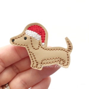 May include: A tan dachshund dog applique wearing a red and white Santa hat. The applique is stitched with brown thread and has black eyes and nose. The text "Fantastic Felties" is visible.