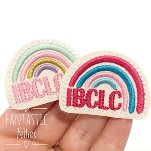 May include: Two white felt rainbow patches with the text "IBCLC" embroidered in pink. The rainbows are multi-colored with pink, blue, green, yellow, and purple.