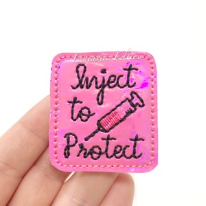 May include: Pink iridescent iron-on patch with black stitching and the text "Inject to Protect" and a black and red embroidered syringe.