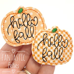 May include: Two felt pumpkin patches with orange and white gingham and polka dot patterns. Both pumpkins have black embroidered text that says "hello fall".