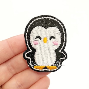 May include: A black and white penguin with a yellow beak and pink cheeks. The penguin is embroidered on a black glitter fabric.