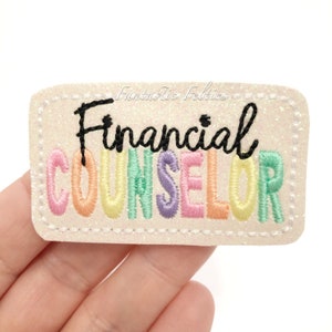 May include: A rectangular patch with the words "Financial Counselor" embroidered in black and pastel colors. The patch has a glittery, off-white background and a stitched border. The text "Fantastic Felties" is written in cursive above the main text.