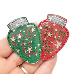 May include: Two Christmas light bulb-shaped ornaments. One is green with red stitching and the words "Let it glow" and star accents. The other is red with green stitching and the same text and star accents. Both have silver tops.