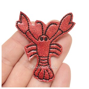 May include: Red glitter lobster applique with black outline. The lobster is facing forward with its claws raised.