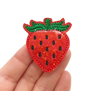 May include: Red and green glitter iron-on patch of a strawberry with black stitching.
