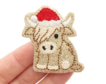 May include: Gold glitter embroidered applique of a sitting cow wearing a red Santa hat.