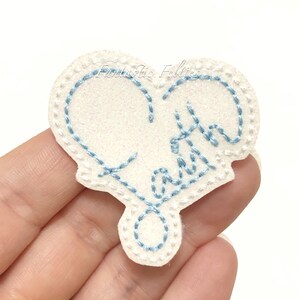 May include: White felt heart with blue embroidery that says "Faith" in a cursive font.