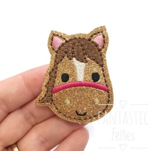 May include: A gold glitter horse head applique with brown hair, pink ears, a white stripe down the nose, and a pink nose band.
