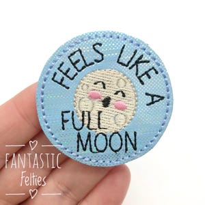 May include: A blue felt patch with a white moon face and the text "Feels like a full moon" in black embroidery.