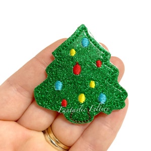 May include: Green glitter Christmas tree applique with red, yellow, and blue embroidered ornaments. The tree has a brown felt trunk with stitching. The text "Fantastic Felties" is visible at the bottom of the tree.