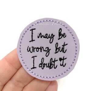 May include: Purple felt circle with the text "I may be wrong but I doubt it" embroidered in black thread.