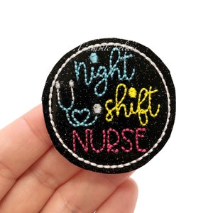 May include: A black and white embroidered patch with the text "night shift nurse" in colorful thread. A stethoscope is embroidered in the upper left corner of the patch.