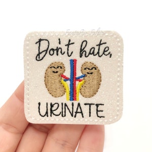 May include: White glitter iron-on patch with black embroidered text that reads "Don't hate, urinate". The patch features a cartoon image of two kidneys with smiling faces and red, blue, and yellow embroidered lines.