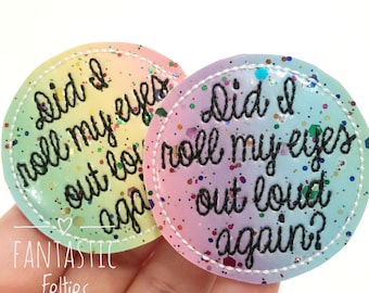 May include: Two round, colorful badges with the text "Did I roll my eyes out loud again?" in black script. The badges have a rainbow gradient background and are sprinkled with glitter. The text "FANTASTIC Felties" is also visible.