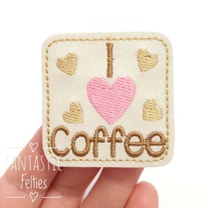 May include: White felt patch with brown stitching and glitter. The patch features a pink heart with the text "I love coffee" in brown.