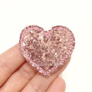 May include: A pink glitter heart with a pink stitched border. The heart is about 2 inches wide.