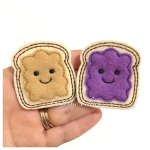 May include: Two felt appliques shaped like slices of bread with smiling faces. One slice is brown and represents peanut butter, the other is purple and represents jelly.