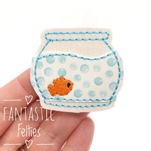 May include: A white felt fishbowl with a blue rim and a small orange felt fish inside. The fishbowl is filled with blue felt bubbles.