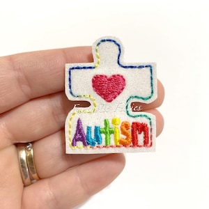 May include: White felt puzzle piece with rainbow embroidery spelling "AUTISM" and a red heart in the center.