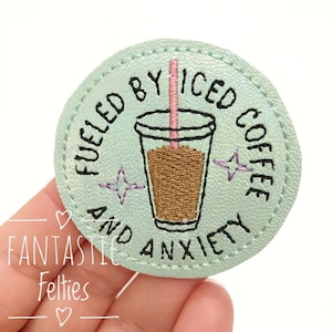 May include: A light green embroidered patch with a circle border. The patch features a cartoon drawing of a cup of iced coffee with a pink straw and the text "Fueled by iced coffee and anxiety".