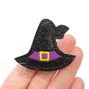 May include: A black witch hat with a purple band and a gold buckle. The hat is covered in glitter and has a pointed crown. The image includes the text "FANTASTIC Felties".