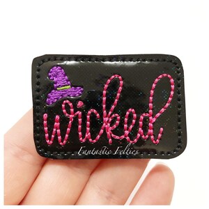 May include: Black rectangular patch with the word "Wicked" embroidered in pink thread. A purple witch hat is embroidered on the left side. The patch has a glossy finish and the text "Fantastic Felties" is at the bottom.