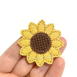 May include: A yellow felt sunflower with a brown felt center. The sunflower has a glittery texture and is outlined with brown stitching.