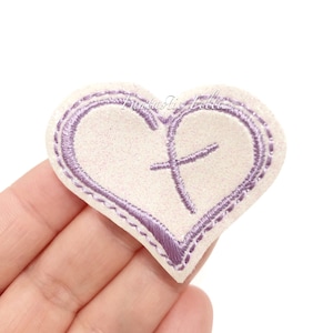 May include: Purple heart-shaped felt patch with a cross inside. The patch is white with a glittery texture.