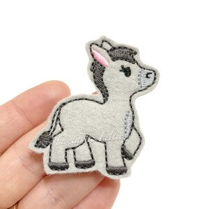 May include: A gray felt donkey applique with black and pink details. The donkey is standing on all four legs and has a friendly expression.