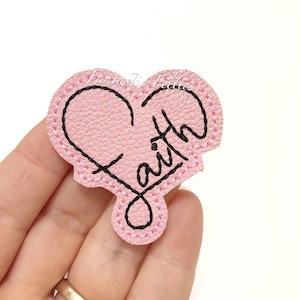 May include: Pink felt heart with black stitching and the word "Faith" written inside.