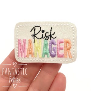 May include: White felt patch with rainbow embroidered text that reads "Risk Manager".