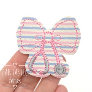 May include: A pink and blue striped felt bow with a gray embroidered stethoscope. The bow is perfect for a doctor or nurse themed craft project.