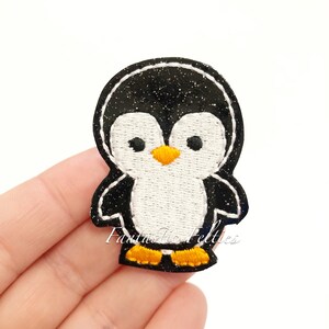 May include: Black and white penguin applique with a yellow beak and feet. The penguin is made of felt and has a glittery black body.