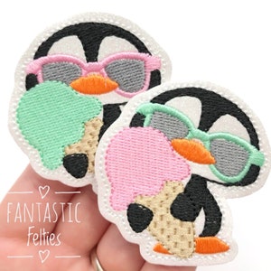 May include: Two embroidered penguin patches, each with a black and white body, wearing sunglasses and holding an ice cream cone. One penguin has pink sunglasses and ice cream, the other has green sunglasses and pink ice cream. The text "Fantastic Felties" is at the bottom.