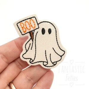 May include: White felt ghost holding a sign that says "BOO" in orange felt letters. The ghost has black eyes and a black outline.
