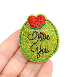May include: A green glittery felt applique in the shape of an olive with a red heart on top. The text "Olive You" is embroidered in black cursive. The applique has a green stitched border.