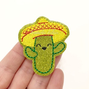 May include: A glittery green cactus patch wearing a yellow sombrero with red trim. The cactus has a smiling face and green arms. The text "Fantastic Follies" is on the sombrero.