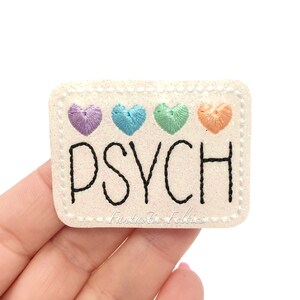 May include: White felt patch with a rainbow of embroidered hearts and the word "PSYCH" in black embroidery.