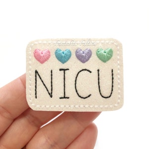 May include: White felt patch with a white glitter background and black embroidered text that reads "NICU". Four embroidered hearts in pink, blue, purple, and green are above the text.