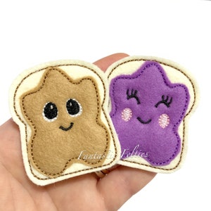 May include: Two felt patches shaped like pieces of bread with smiling faces. One piece of bread has a brown peanut butter filling shaped like a star. The other piece of bread has a purple jelly filling shaped like a star. The text "Fantastic Felties" is visible on the image.
