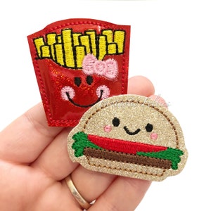 May include: Two felt food patches, a red and yellow french fry container with a smiling face and a pink bow, and a gold glitter hamburger with a smiling face.