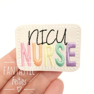 May include: A white felt patch with the words "NICU NURSE" embroidered in rainbow colors. The letters are outlined in black.